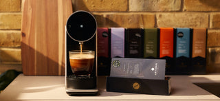 Artisan Coffee Co coffee pods are surrounding a light blue ceramic espresso cup that has a teaspoon with it